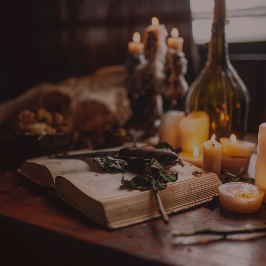An open book rests on wood amid candles, dried leaves, and a glass bottle, creating a mystical vibe—perfect for Spellcrafter’s Virtual Yule Ritual on December 22nd at 6 PM.