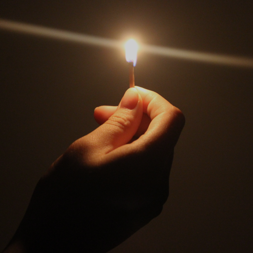 A hand holding a lit matchstick in the dark evokes the feeling of sitting in the power—connecting to the spirit world, like at Spellcrafter’s “Sitting in the Power: Learn to Connect to the Spirit World,” Nov 18th, 6:30 PM.