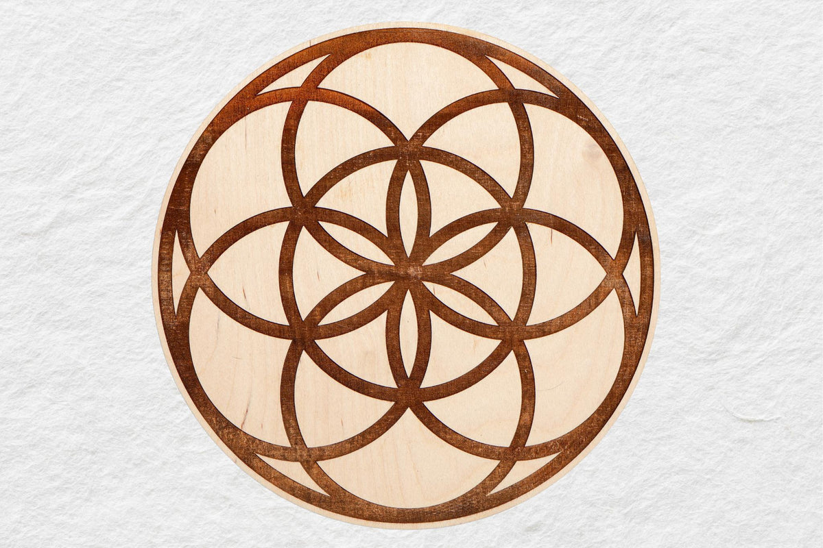 The Spellcrafter 8" Wood Seed of Life Grid features a circular, intricately layered arc and oval pattern inspired by sacred geometry, resembling a Seed of Life crystal grid on a light textured background.