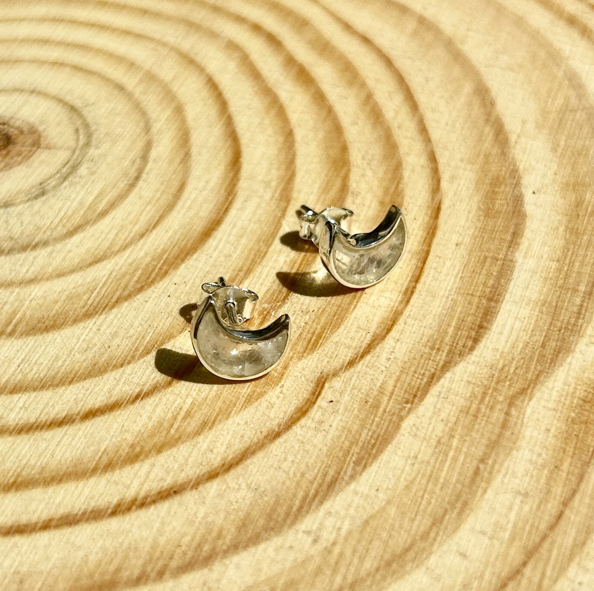 A pair of Spellcrafter Rainbow Moonstone Butterfly Sterling Silver Stud Earrings displayed on a light wooden surface with circular ring patterns.