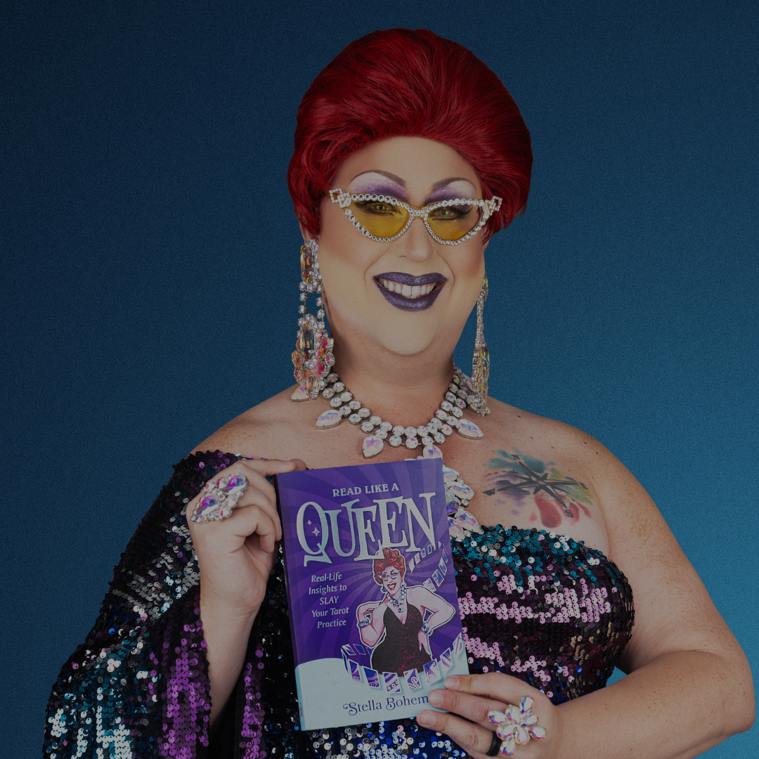 A glamorous person with red hair, bold makeup, yellow sunglasses, and sparkling jewelry smiles while holding Spellcrafter’s Reading with Stella Boheme book, ready for a tarot event in Central Florida against a blue background.