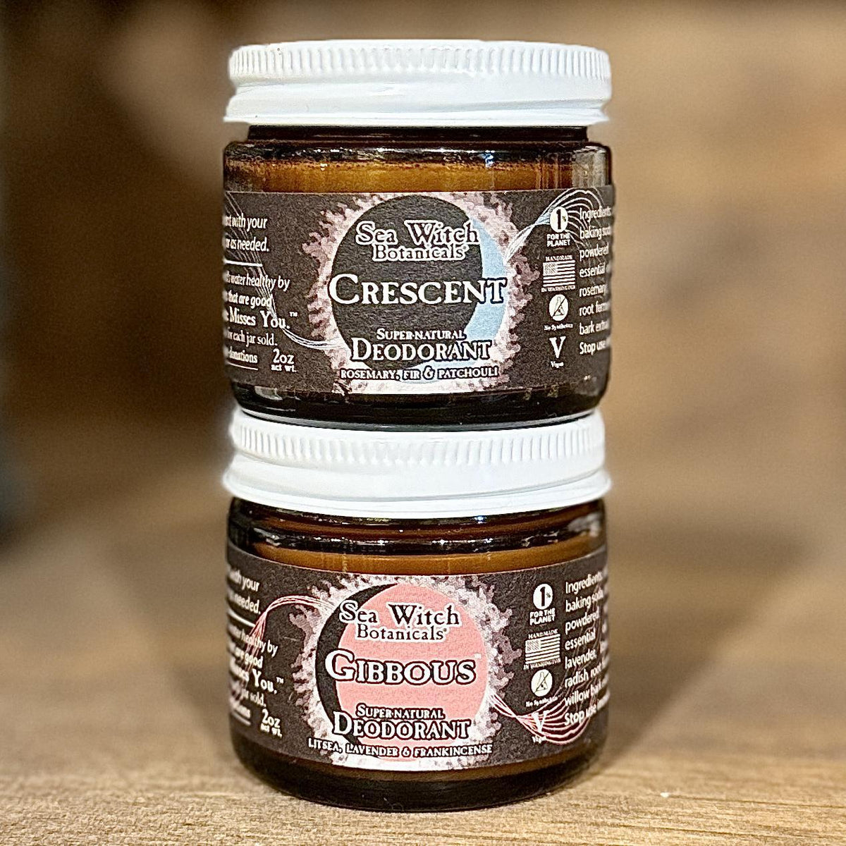Two brown glass jars of Spellcrafter SuperNatural Deodorant are stacked. The top jar is Crescent with rosemary and patchouli; the bottom is Gibbous with lavender and frankincense. Both are zero waste deodorants.