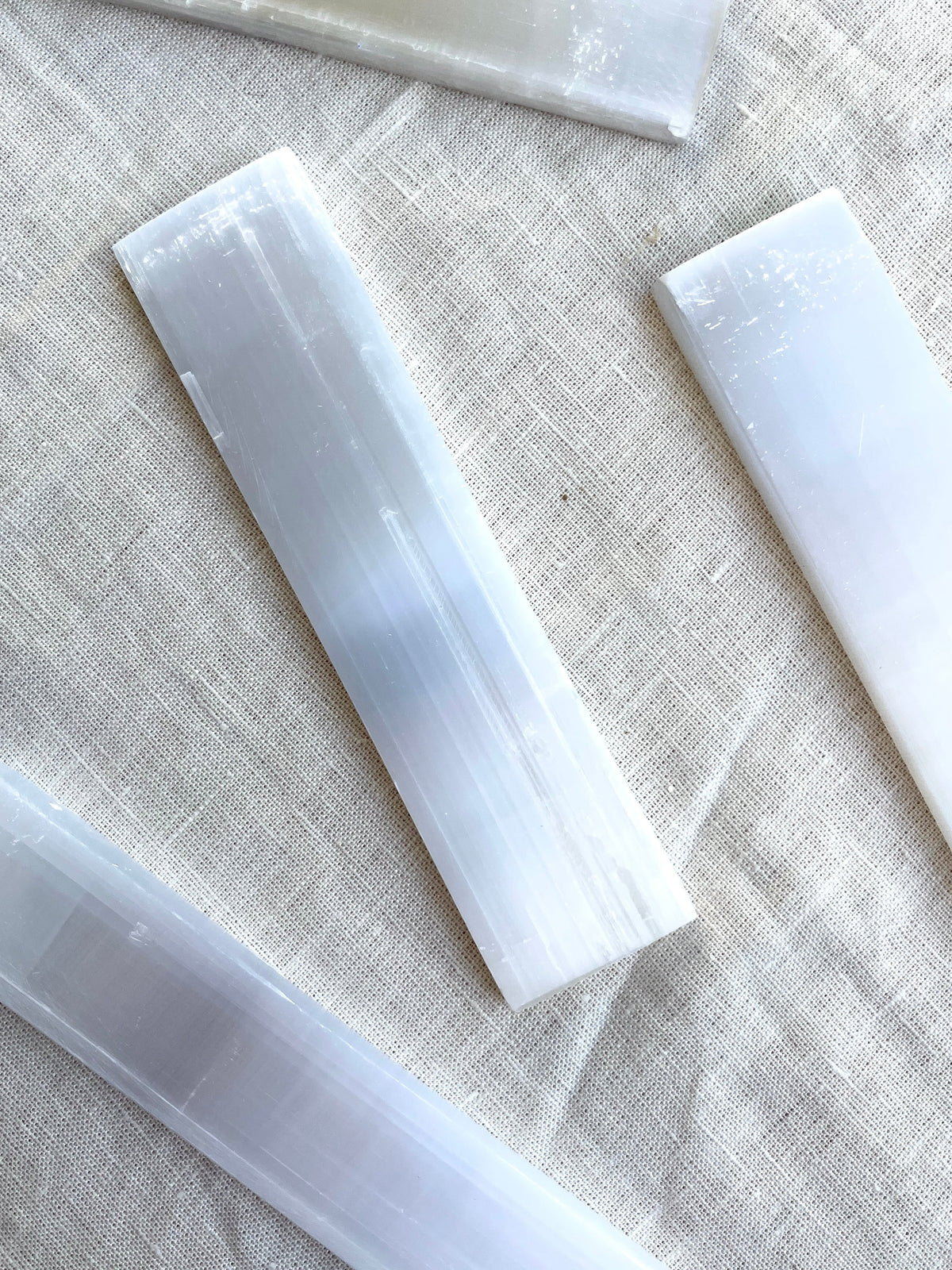 Spellcrafter Selenite Bars are displayed on a light textured fabric background, ideal for cleansing or charging crystals and creating a simple, serene atmosphere.