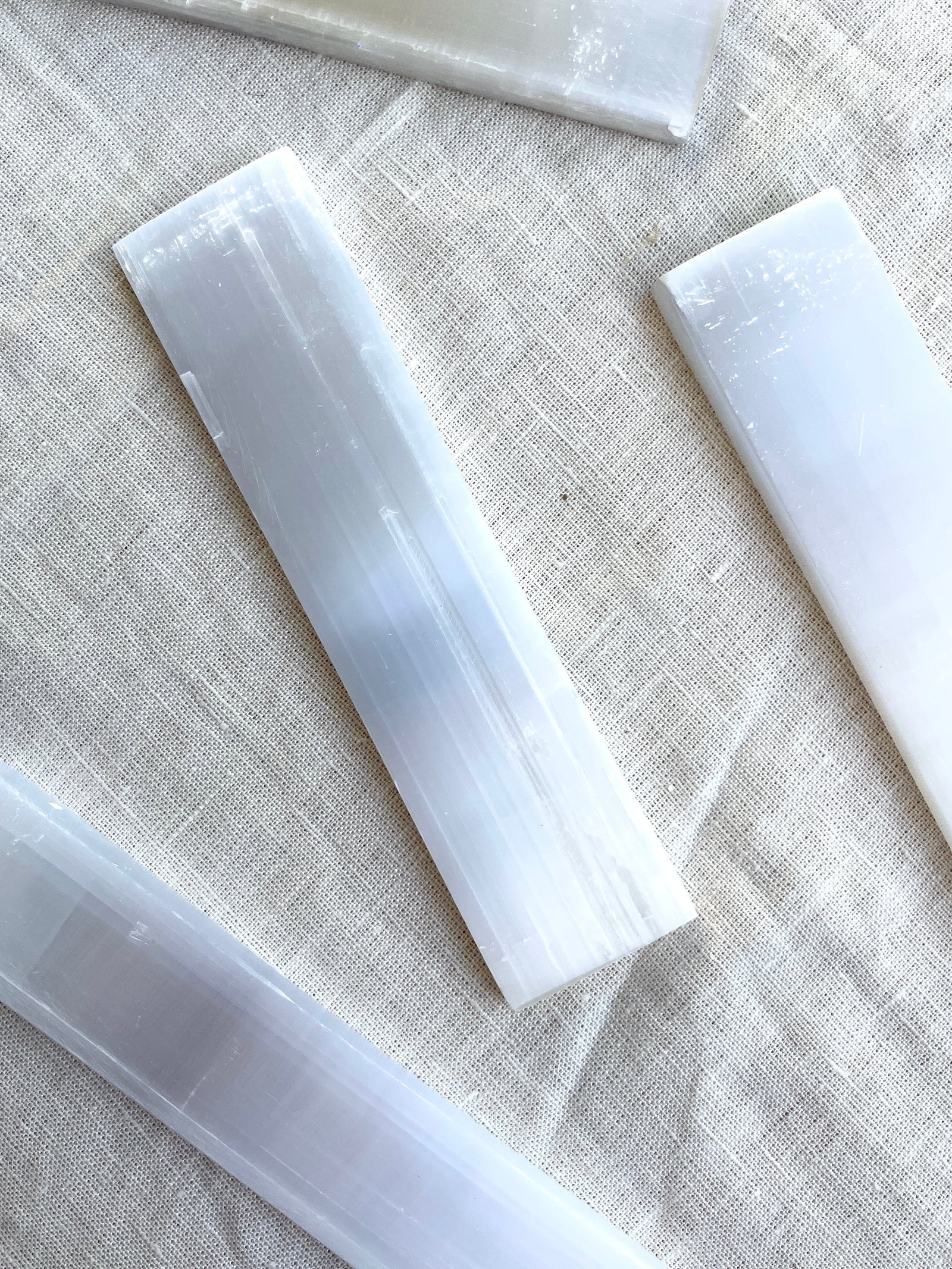 Spellcrafter Selenite Bars are displayed on a light textured fabric background, ideal for cleansing...