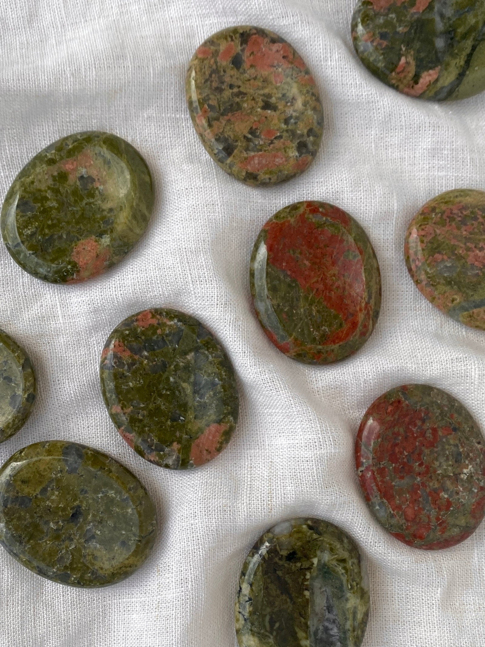 Oval, polished Spellcrafter Unakite Calming stones featuring green and reddish-pink patterns are displayed on...