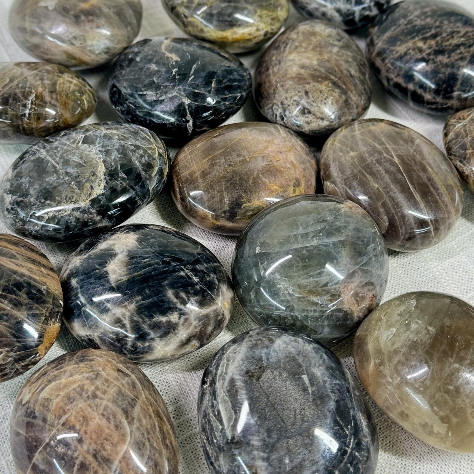 Spellcrafter's Black Moonstone Palm Stone Intuitively Chosen features polished, oval-shaped grounding stones with gray,...