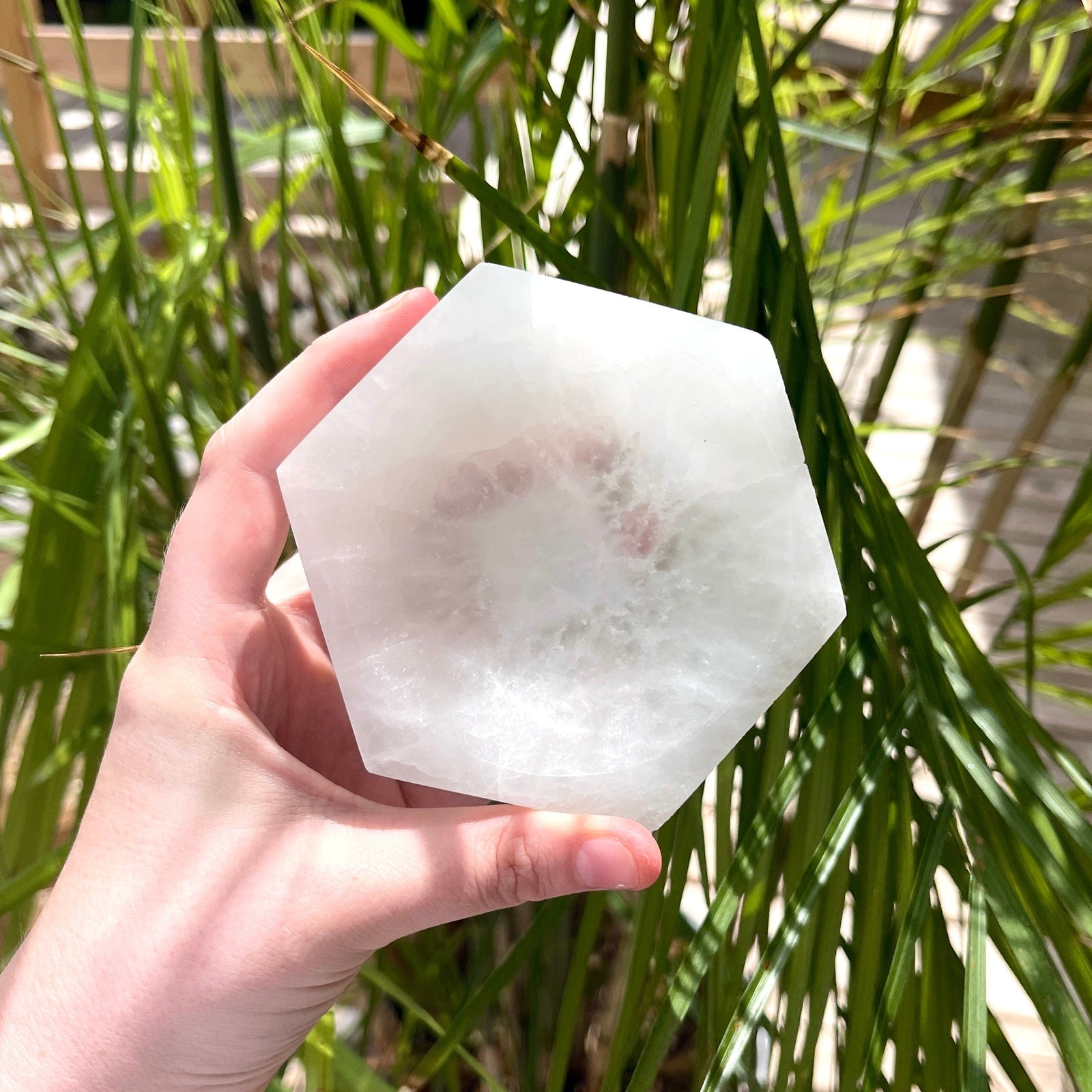 A hand holds the Spellcrafter Hexagon Selenite Bowl—a large, translucent white crystal bowl ideal...