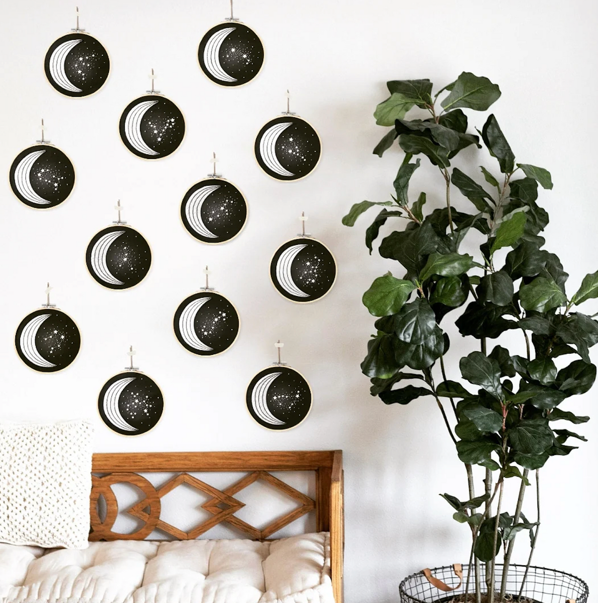 A wall with black and white moon phase art above a wooden bench and tall leafy plant creates a creative space—ideal for showcasing your Spellcrafter XEmbroidery Kit.