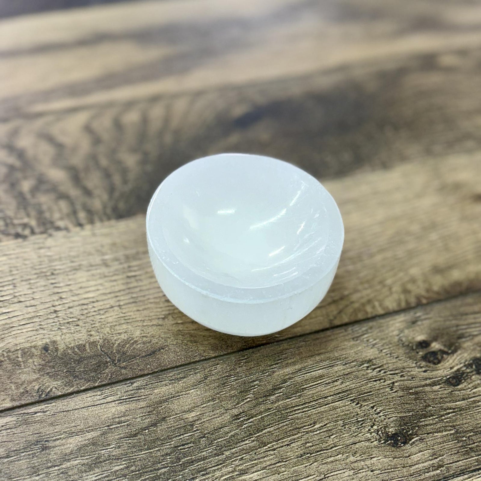 The Spellcrafter Selenite Round Mini Bowl, a translucent white piece, rests on a textured...