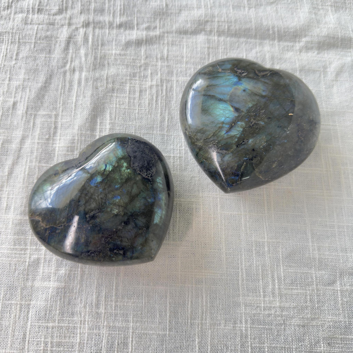 Two Spellcrafter Labradorite Heart stones rest on a white surface, ideal for balancing chakras and inspiring creativity.
