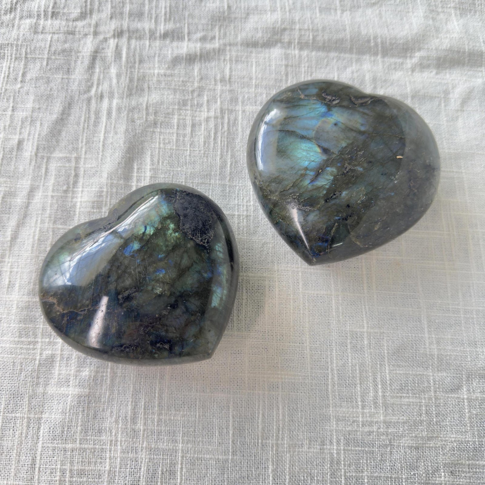 Two Spellcrafter Labradorite Heart stones rest on a white surface, ideal for balancing chakras...