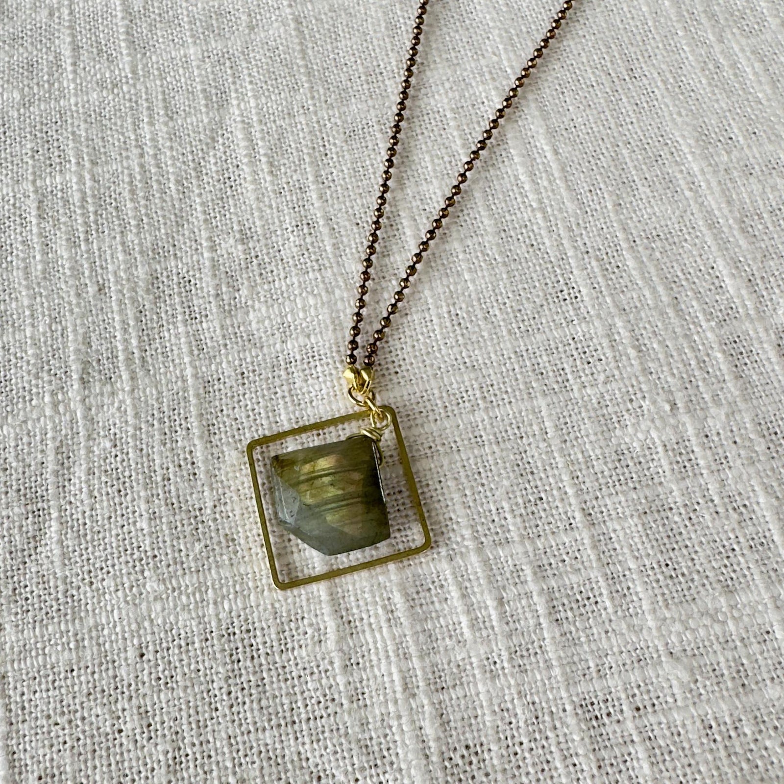 The Spellcrafter Labradorite Framed Diamond Necklace features a square, gold-framed greenish-gray labradorite pendant on...