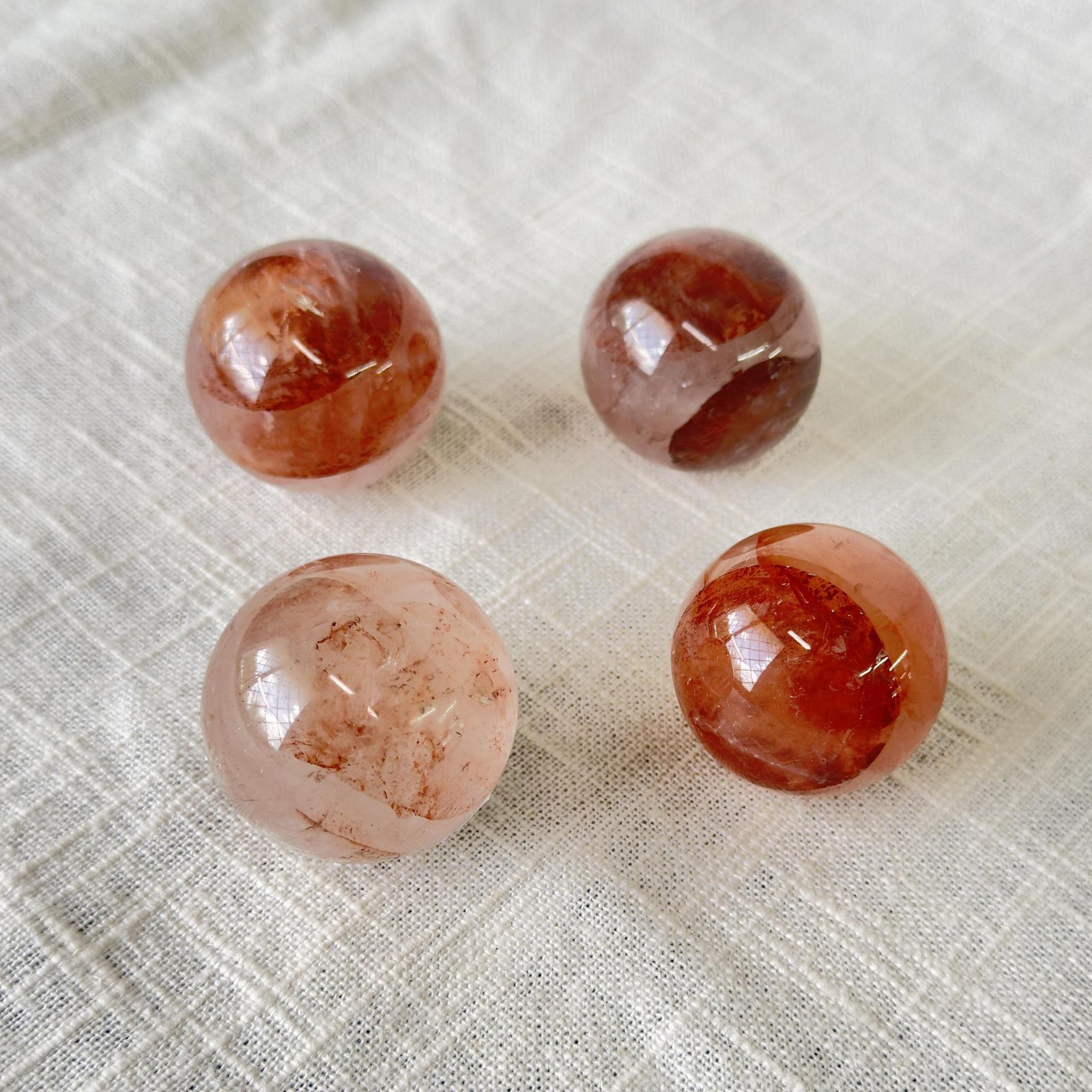 Four Spellcrafter Fire Quartz Spheres in reddish-brown and pink rest on a textured white...