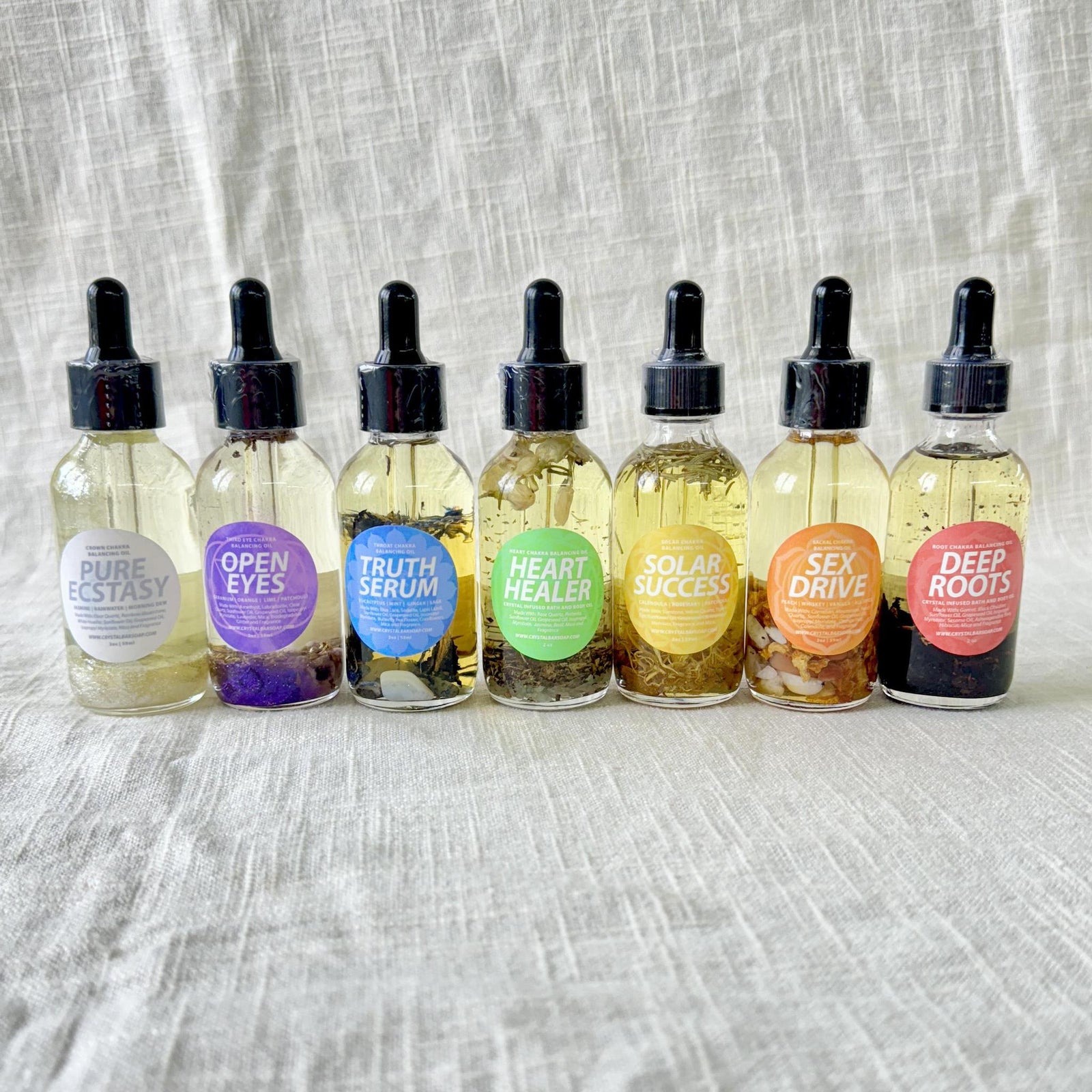 Seven Spellcrafter Chakra Balancing Oil glass dropper bottles, each with a colorful label and...