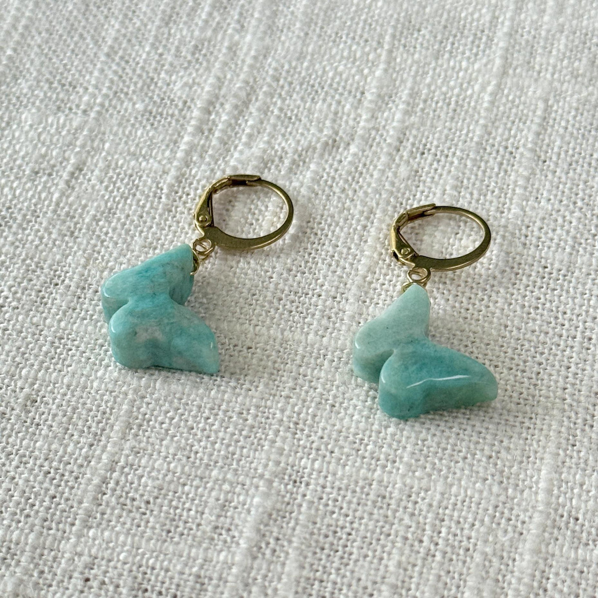 Two Spellcrafter Amazonite Butterfly Earrings with gold hoops and light blue butterfly-shaped pendants are shown on textured white fabric.