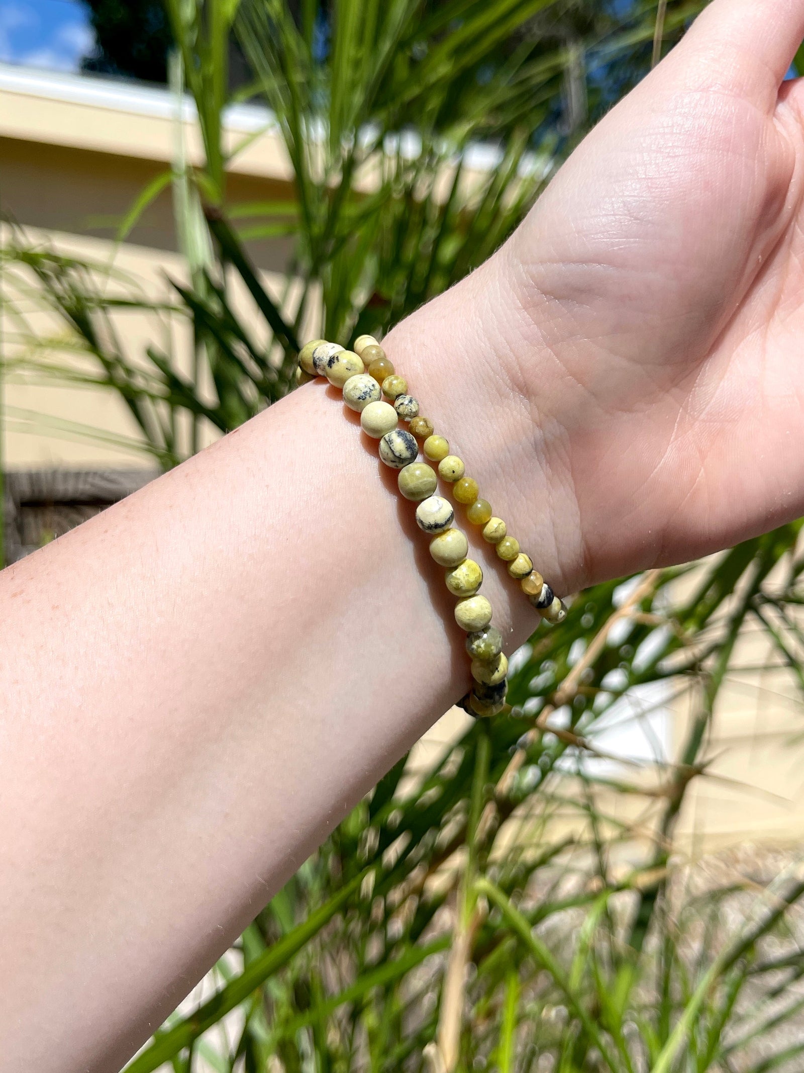 A hand wearing two Spellcrafter Yellow Agate Bracelets is raised outdoors in sunlight, with...